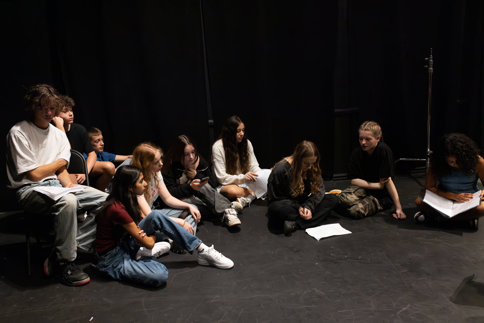 A group of students study scripts while listening in a theatre and sitting on the stage floor during acting classes in Dubai