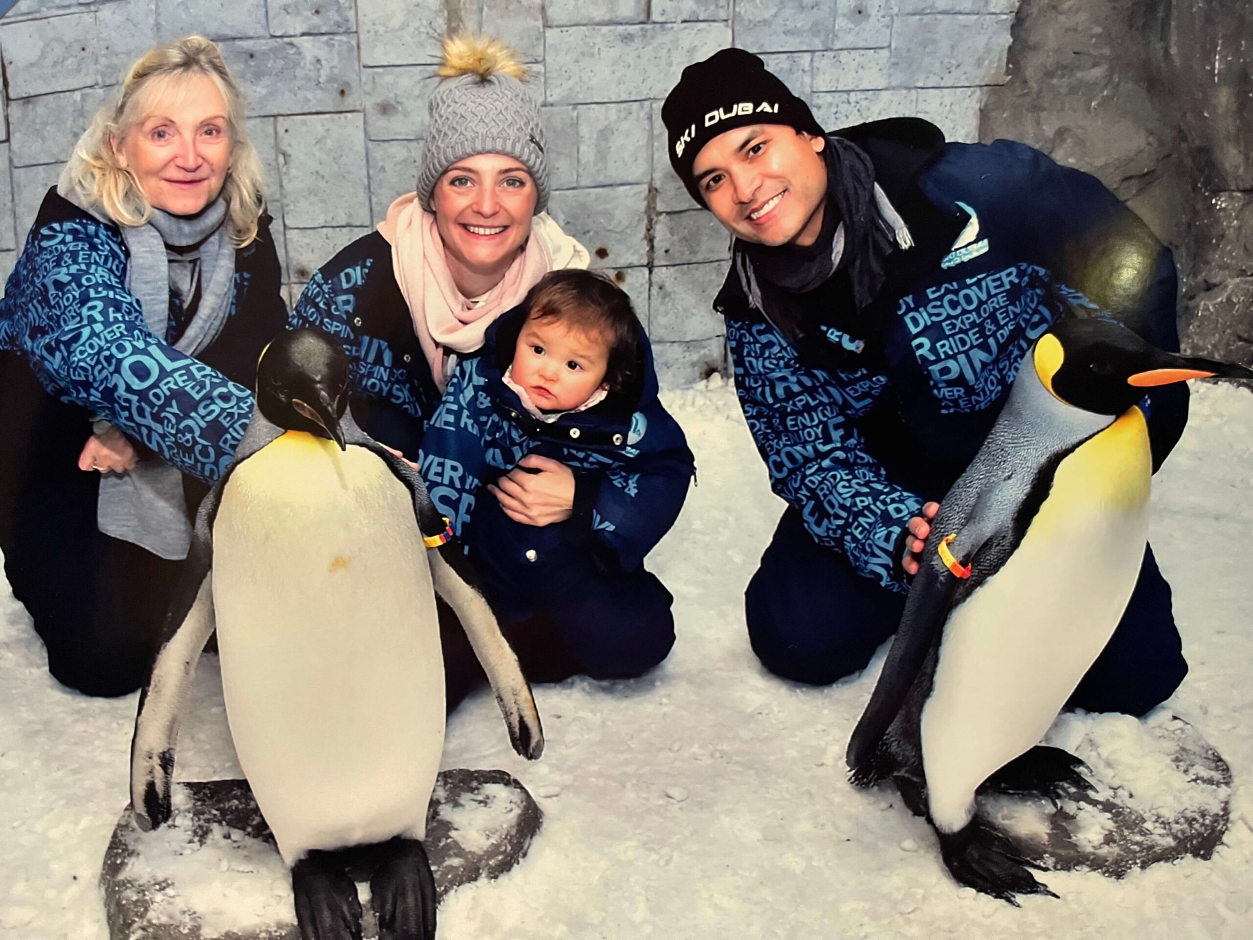 Happy mom, dad and grandma introduce their baby to penguins in the penguin meet and greet petting zoo at Ski Dubai